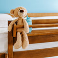 Plush beige teddy bear sitting on a wooden bed rail next to a blue sippy cup in a cozy toddler bedroom nursery