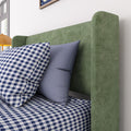 Green upholstered headboard with blue pillows and blue-and-white gingham bedding in a modern bedroom featuring a yellow bedside lamp