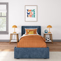 Kids bedroom with blue upholstered bed, orange quilted bedding, framed "Young Wild and Free" wall art, matching orange table lamps and nightstands
