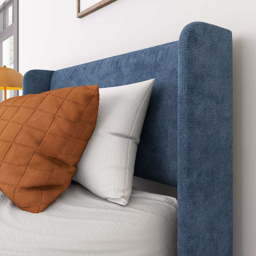 Blue upholstered bed with white and orange pillows in modern bedroom setting.