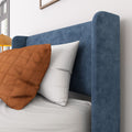 Close-up of blue upholstered headboard with textured fabric, white pillows and rust-orange decorative pillow in a modern bedroom interior
