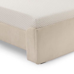 Close-up of beige upholstered platform bed corner with quilted white mattress topper and fabric bed base