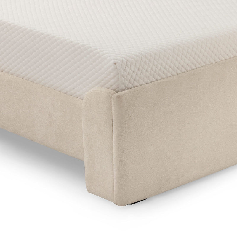 Close-up of beige upholstered platform bed corner with quilted white mattress topper and fabric bed base