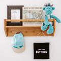 Nursery wall shelf decor with "Where the Wild Things Are" children's book, framed art, blue plush dragon toy, hanging baseball cap and "Long Live Boyhood" banner.