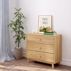 Pine wood dresser with books and plant, modern minimalist bedroom decor.
