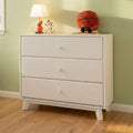 White mid-century modern three-drawer dresser chest of drawers for nursery or bedroom, styled with a lamp and plush basketball on a hardwood floor against a pale green wall