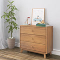 Mid-century modern three-drawer wooden dresser in bright nursery with potted plant, framed children's art, toy sailboat and stacked books on hardwood floor