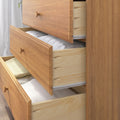 Light wood bedroom dresser with three open drawers showing neatly folded linens and towels, natural oak finish, modern storage solution