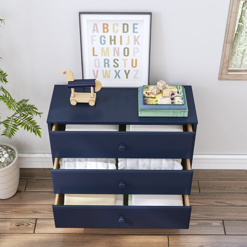Navy blue three-drawer nursery dresser with folded baby clothes inside, wooden toy horse and stacked children's books on top, pastel framed alphabet poster, potted plant and hardwood floor — kids room storage and nursery decor