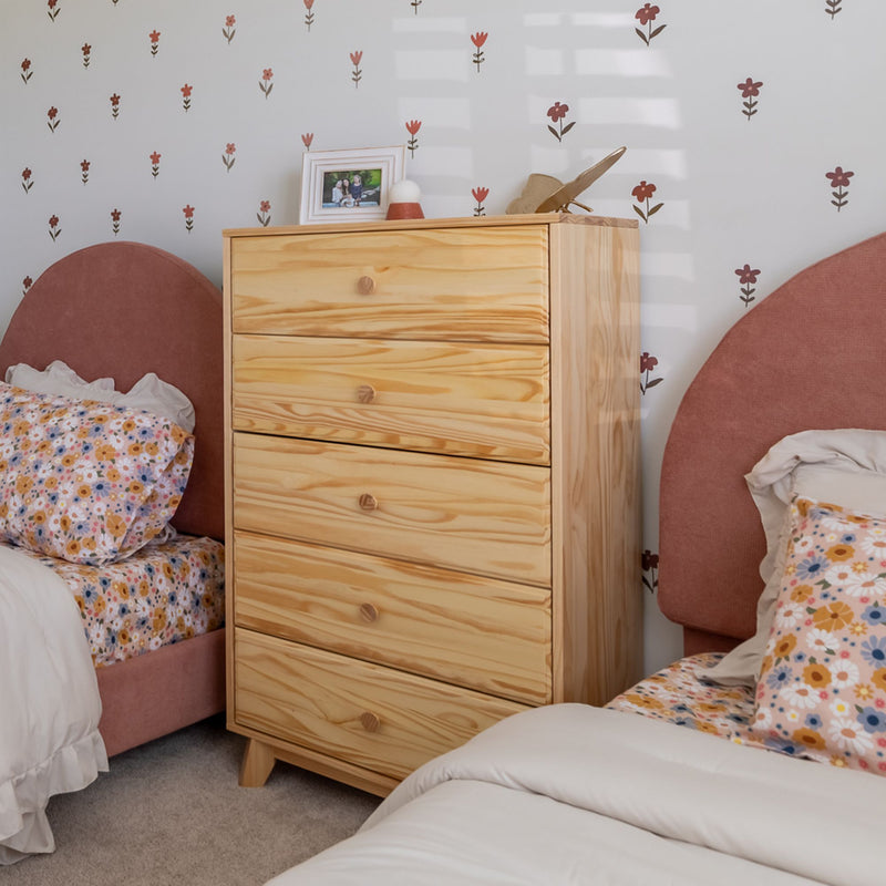 Cozy kids' bedroom with twin beds, pink upholstered headboards, floral bedding, a light pine five-drawer dresser, framed photo and flower wall decals