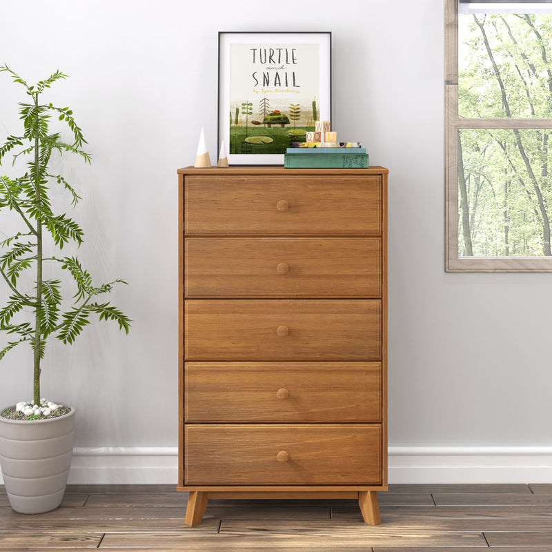 Mid-century modern five-drawer wooden dresser in natural oak finish staged in a bright bedroom with potted plant, framed turtle print and window view