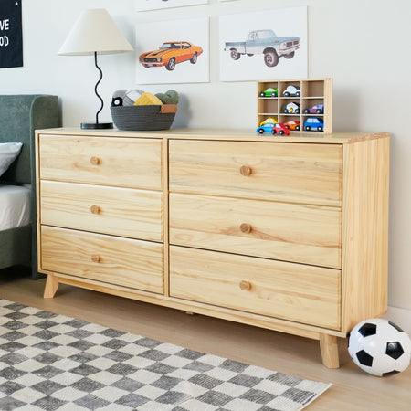 Natural wood dresser with six drawers, kids' toys, and decor in a bedroom setting with framed car artwork and a cozy rug.