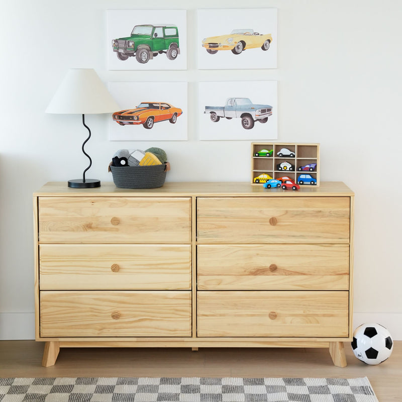 Children's room with wooden dresser, toy cars, soccer ball, and wall art of vintage cars.