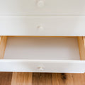 Open white dresser drawer with round knob, empty pine interior on hardwood floor, minimalist bedroom storage