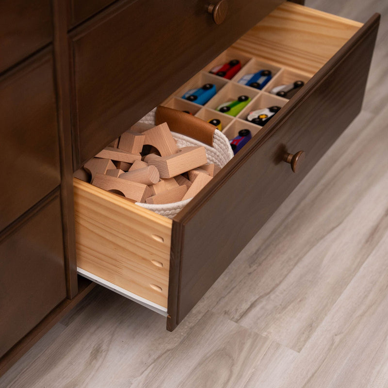 Open dark wood dresser drawer in child's room with wooden building blocks in a rope basket and divided toy car organizer on light laminate floor