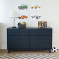 Navy blue six-drawer dresser in kids' bedroom with lamp, toy basket, wooden toy car organizer, car-themed wall art, soccer ball and checkered rug