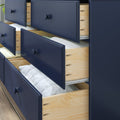 Modern navy blue dresser with multiple open wooden drawers showing folded white linens and blankets, bedroom storage and organization solution