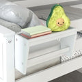 White wooden bed-mounted bedside shelf holding stacked pastel books and a smiling avocado plush, modern kids' bedroom storage and decor