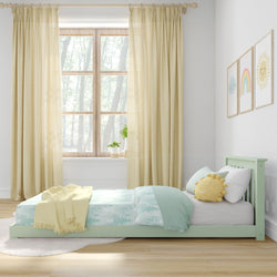 Cozy children's bedroom with pastel green bed frame, cheerful sun cushion, and pastel decor.