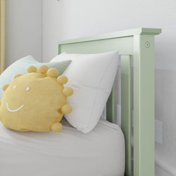 Pastel green crib with yellow smiling sun pillow and comfortable white bedding, perfect for a cozy nursery.