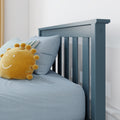 Blue wooden toddler bed headboard with vertical slats, light-blue bedding and striped pillow, yellow sun plush toy in a modern nursery interior