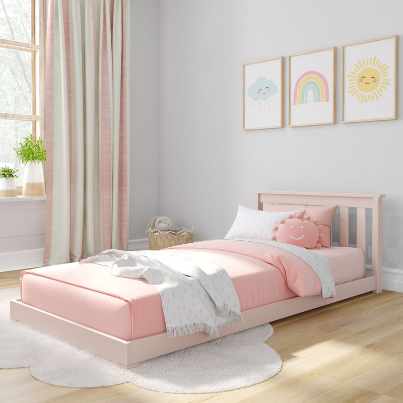 Pastel pink toddler bed and bedding in cozy nursery with smiling sun, rainbow and cloud wall art, blush curtains and potted plants
