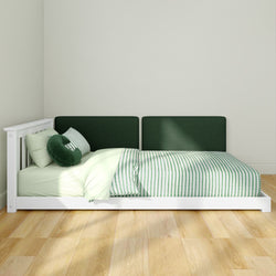 Low white wooden platform bed with dark green upholstered headboard, green-striped duvet and pillows in a minimalist bedroom with natural light and light hardwood floor.