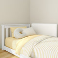 White wooden children's bed with yellow striped duvet, matching pillows and crescent cushion in a minimalist nursery with light hardwood floor