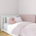 Pink striped nursery bedding in a white baby crib with a soft pink U-shaped pillow and upholstered headboard, modern baby nursery decor