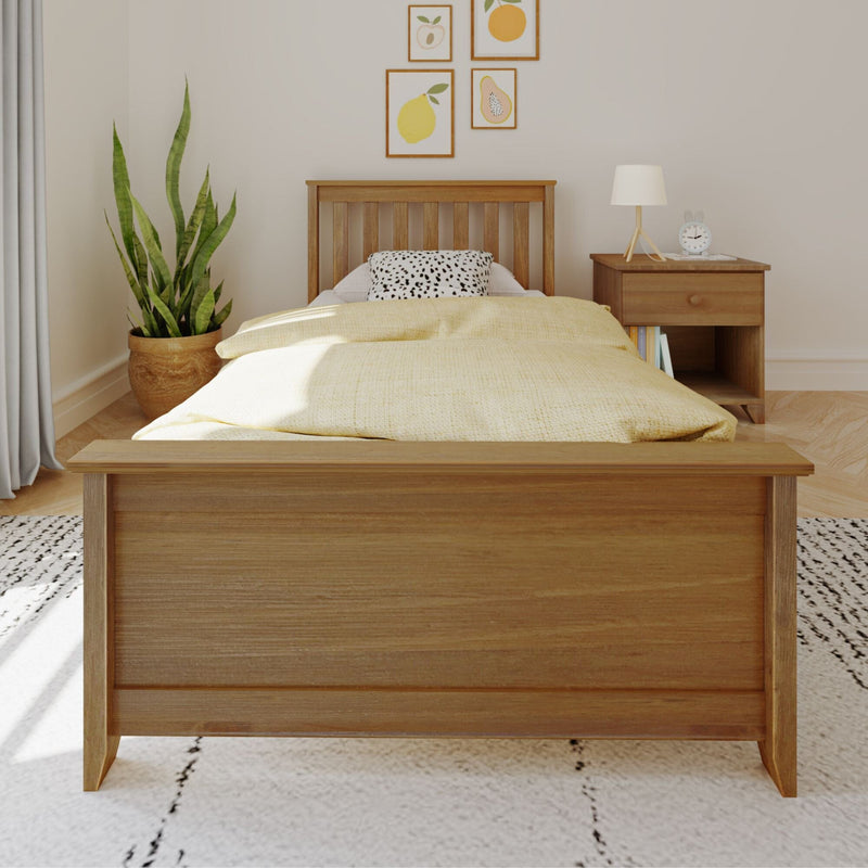 Minimal Scandinavian bedroom with wooden bed frame, yellow bedding and spotted pillow, wooden nightstand with lamp and alarm clock, potted snake plant and fruit-themed wall art on neutral walls.