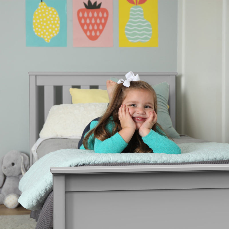 Smiling child lying on a gray bed in a cozy bedroom with colorful wall art.