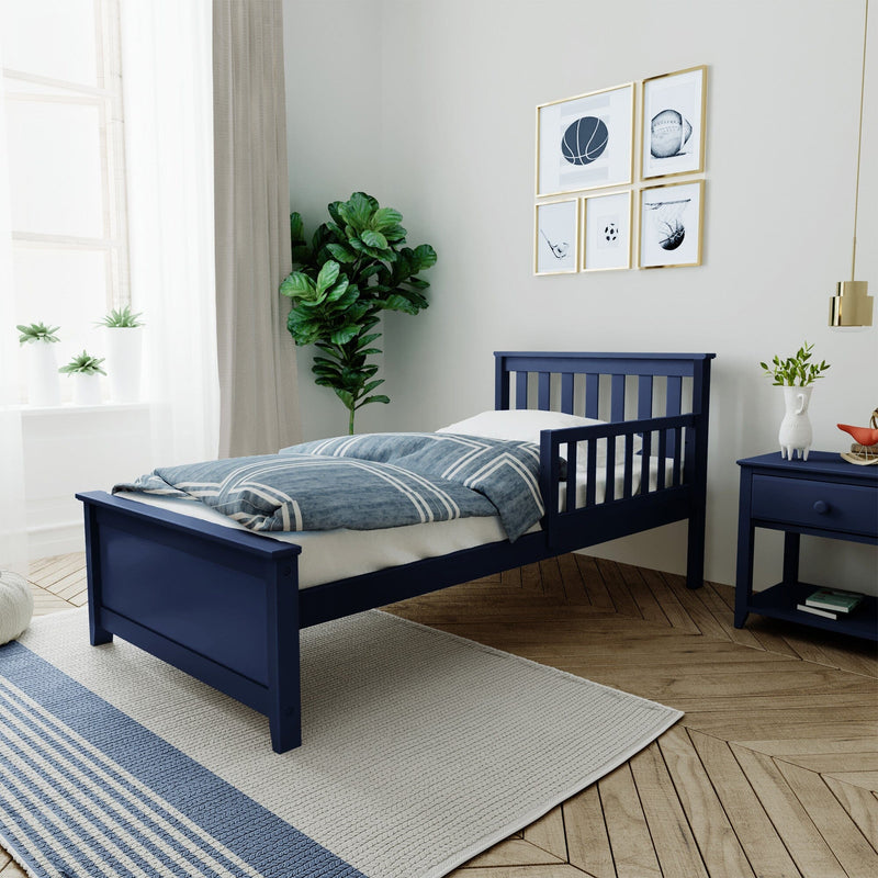 Modern navy blue kids bed with striped blue bedding in a bright children's bedroom featuring a navy nightstand, fiddle leaf fig plant, white sheer curtains and sports-themed gallery wall art