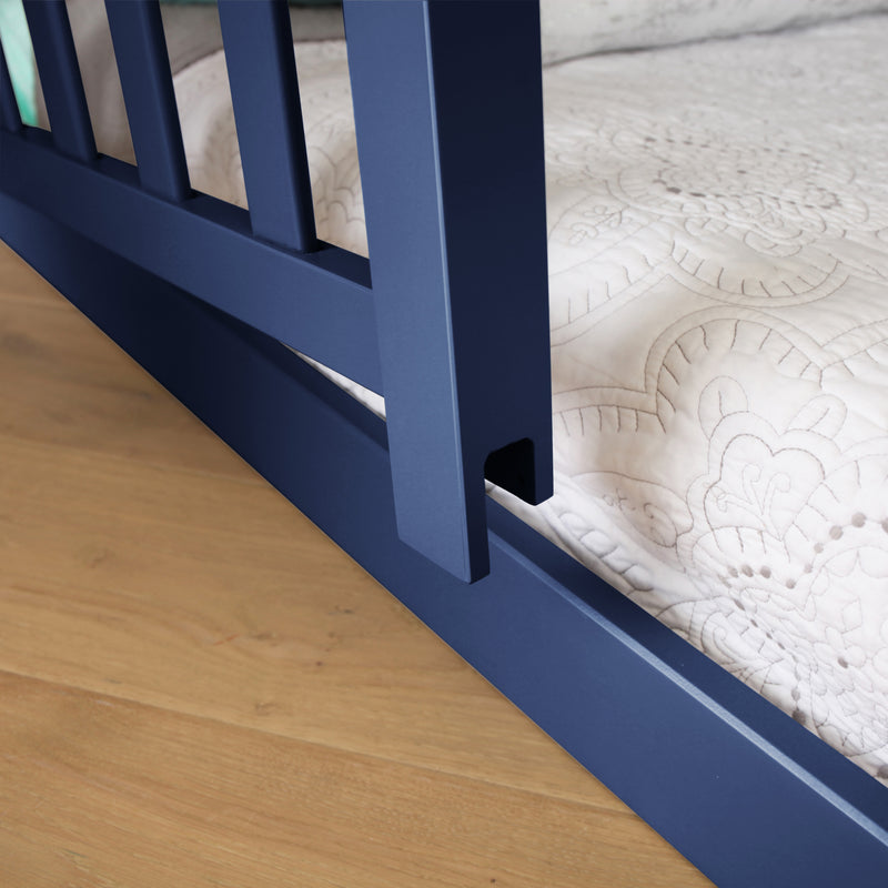 Blue metal crib rail next to white patterned bedding on wooden floor.