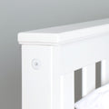Close-up of white painted wooden crib rail and headboard detail with visible screw cap, modern nursery bed furniture