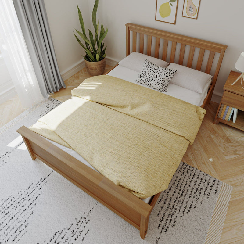 Minimalist modern bedroom with wooden bed frame, yellow duvet and patterned pillow, potted snake plant, natural light and framed fruit prints
