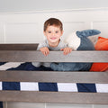 Smiling child on gray wooden bunk bed with navy and white striped bedding and plush whale pillow, kids bedroom decor and children's furniture