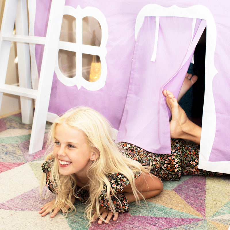 Smiling blonde girl playing in a purple kids play tent on a colorful patterned rug