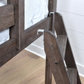 Wooden bunk bed ladder with metal safety hooks attached to a gray-brown wood bed frame, showing wood grain and hardwood bedroom flooring
