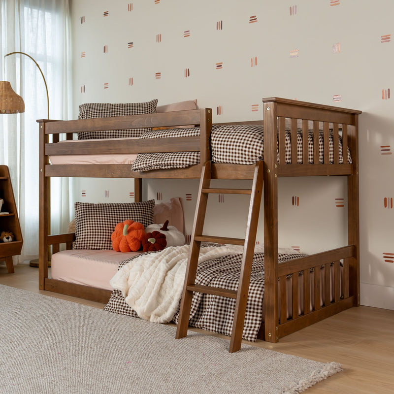 Wooden twin-over-twin bunk bed with ladder in cozy kids bedroom, brown gingham bedding, pink sheets, plush pumpkin pillows and neutral dot-pattern wall decor