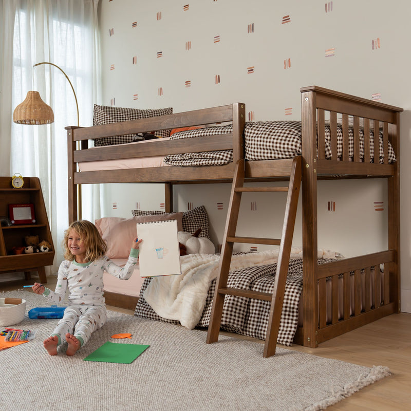 Wooden twin-over-twin bunk bed in cozy children's bedroom with ladder, gingham bedding, plush rug, bedside shelf and child drawing on floor with art supplies