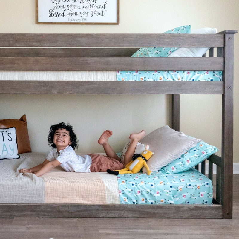 Child smiling on lower bunk bed with colorful bedding and stuffed toy, ideal for family homes and children's bedrooms.