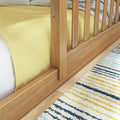 Close-up of natural oak slatted bed frame and footboard with yellow bedding on hardwood floor and striped woven rug