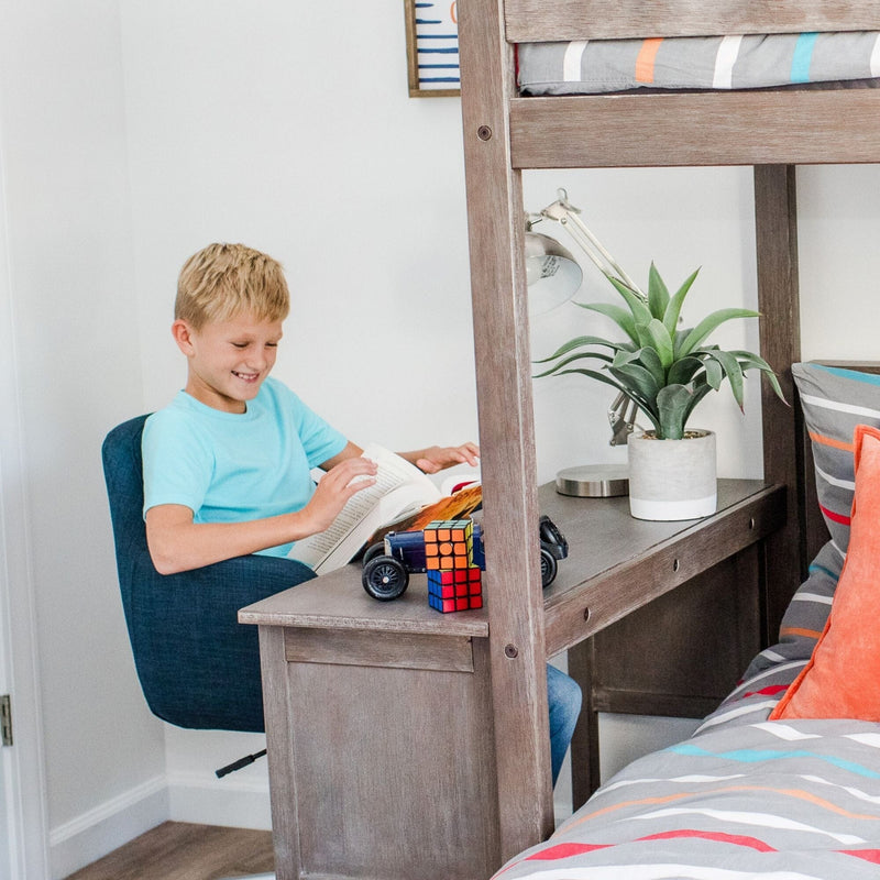 Boy reading a book at a wooden desk built into a bunk bed in a colorful kids' bedroom study nook with a Rubik's Cube, toy car, potted plant, and desk lamp.