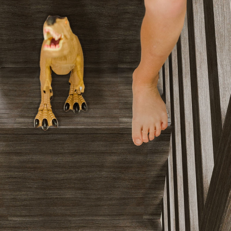Toy T-Rex dinosaur on dark wooden stairs next to a bare foot, close-up indoor play scene