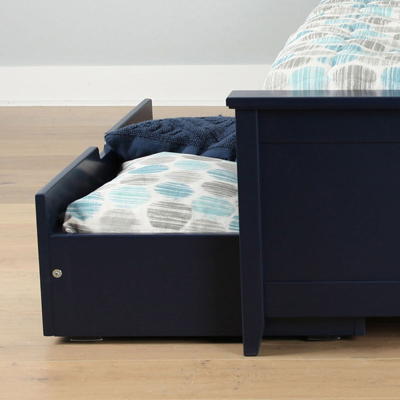 Modern navy blue wooden bed frame with pull-out underbed trundle storage drawer, patterned blue-gray pillows on hardwood floor