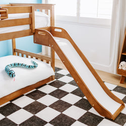 Wooden kids bunk bed with attached slide in bright children's bedroom with black-and-white checkered rug and blue plush snake toy