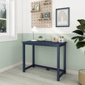 Minimalist home office corner with navy narrow writing desk under natural light, white desk lamp, succulent, pencil holder, pegboard shelves and framed rainbow wall art