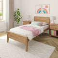 Cozy pastel bedroom with wooden bed, white textured bedding, pink throw blanket, pastel rainbow wall art, potted plant and matching bedside lamps