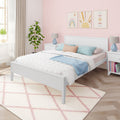 Pastel pink bedroom with white bed, blue and peach pillows, scallop-pattern wallpaper and framed rainbow and sun art, bedside lamps and indoor plant
