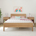 Modern bedroom interior with wooden platform bed, white quilted comforter, pastel pink and mint pillows, matching wooden nightstands with pink geometric lamps, potted plant, bunny alarm clock, and two framed rainbow prints on cream patterned wallpaper